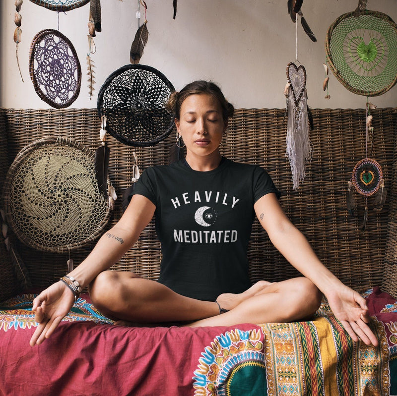Women meditating wearing black t-shirt with white HEAVILY MEDITATED graphic and a white moon in the center