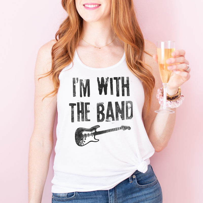 Woman holding champagne, wearing a white rocker racerback tank top with  a distressed  black guitar graphic on the front, and distressed black lettering that says 'I'M WITH THE BAND'