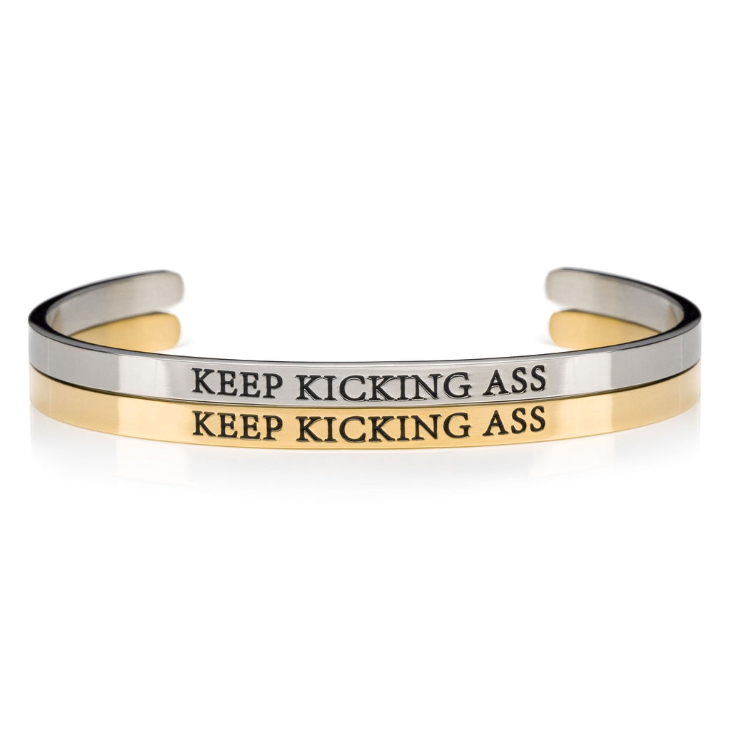 1 silver and 1 gold open cuff bracelet that says KEEP KICKING ASS in black lettering