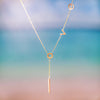 Gold lariat necklace with lowercase latters spelling "love". Necklace hanging in front of sunset