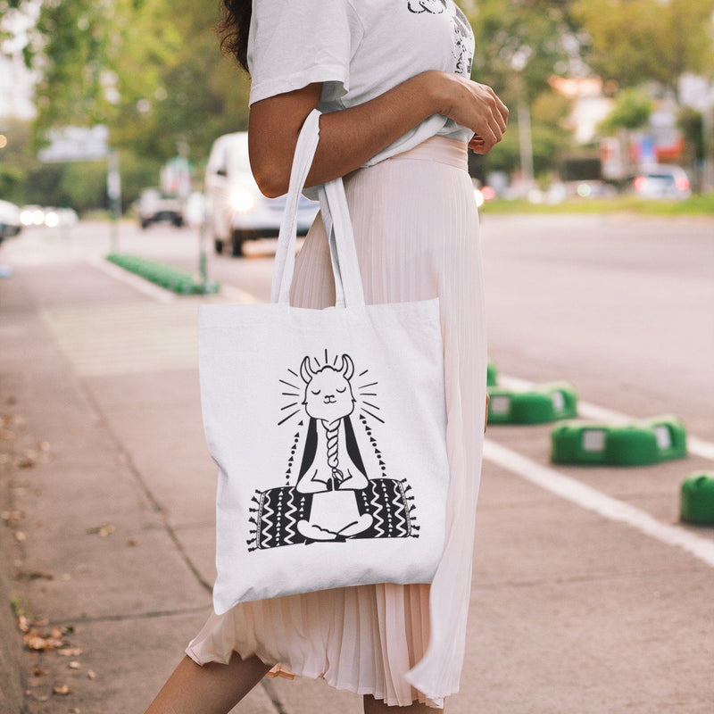 White canvas tote bag with black graphic of a meditating llama sitting cross-legged doing yoga