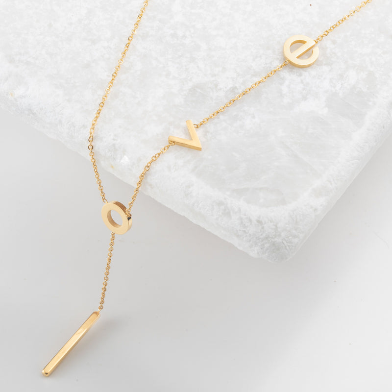 Gold lariat necklace with lowercase latters spelling "love"