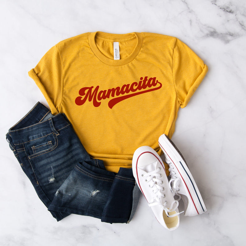 Yellow t-shirt with red cursive mamacita graphic paired with jeans and white sneakers