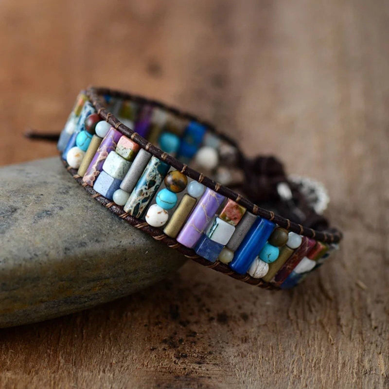Multi-colored jasper and agate gemstone beaded bracelet on dark brown leather cording, leaning on a rock