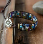 Multi-colored gemstone beaded chakra bracelet made with dark brown leather cord with silver sunflower button closure