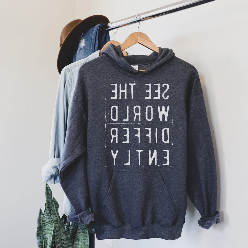 See the world differently printed in White Reverse letters on dark heather gray hooded sweatshirt on hanger
