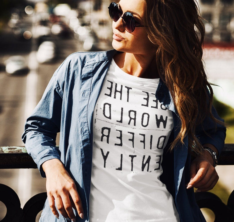 Woman in sunglasses wearing White T-shirt with reverse black letters that say See The World Differently backwards